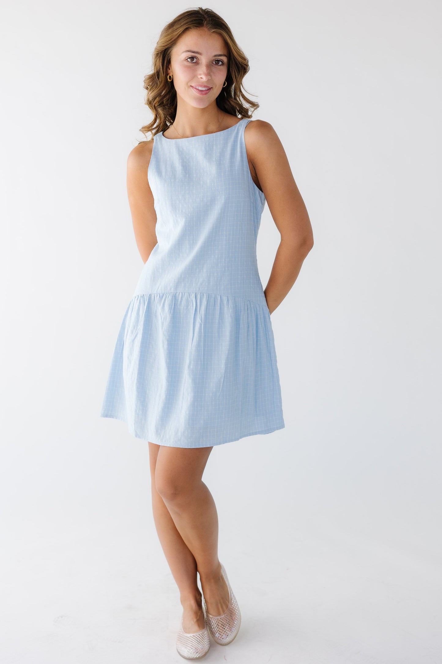 Young woman wearing a light blue plaid sleeveless dress with a drop waist and round neckline.