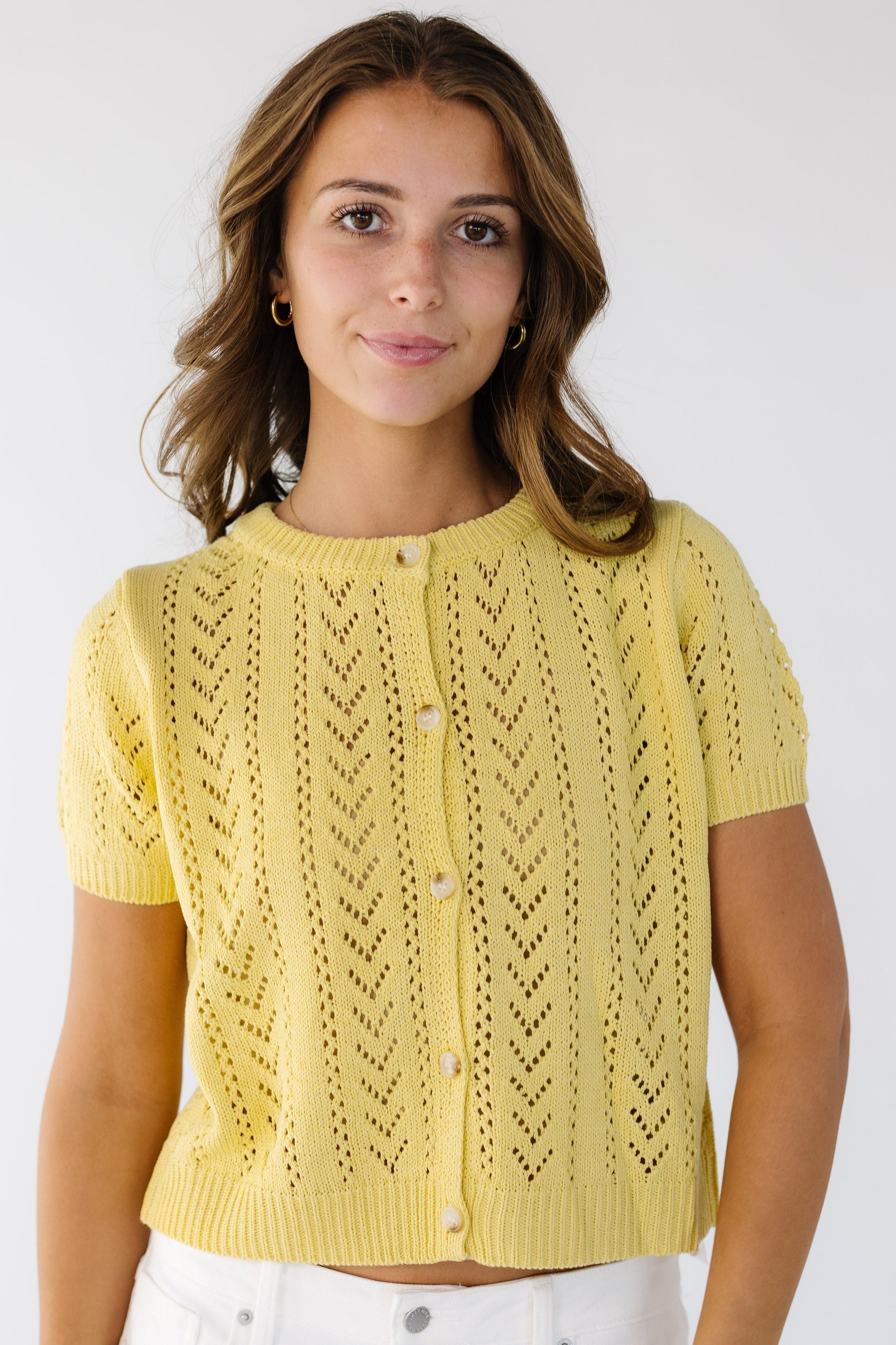 Woman wearing a lacey knit cardigan in yellow that buttons down the front with short sleeves.