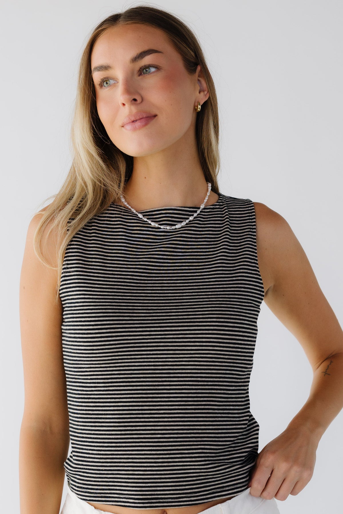 Woman wearing a close fitting tank top in beige and black narrow stripes with a round neckline.