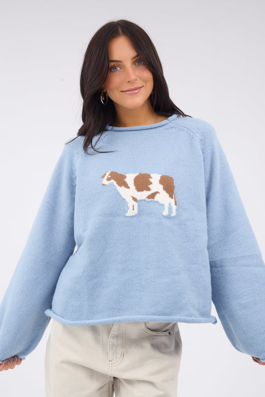 A young woman wearing a modest light blue pullover with a lfarge front cow graphic with side sleeves and rolled hems.