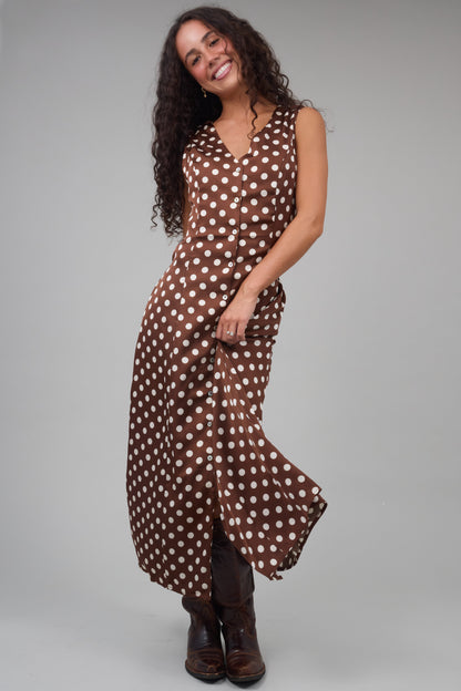 Young woman wearing a sleeveless brown & cream polka dot, button down dress with a v-neckline and A-line skirt.