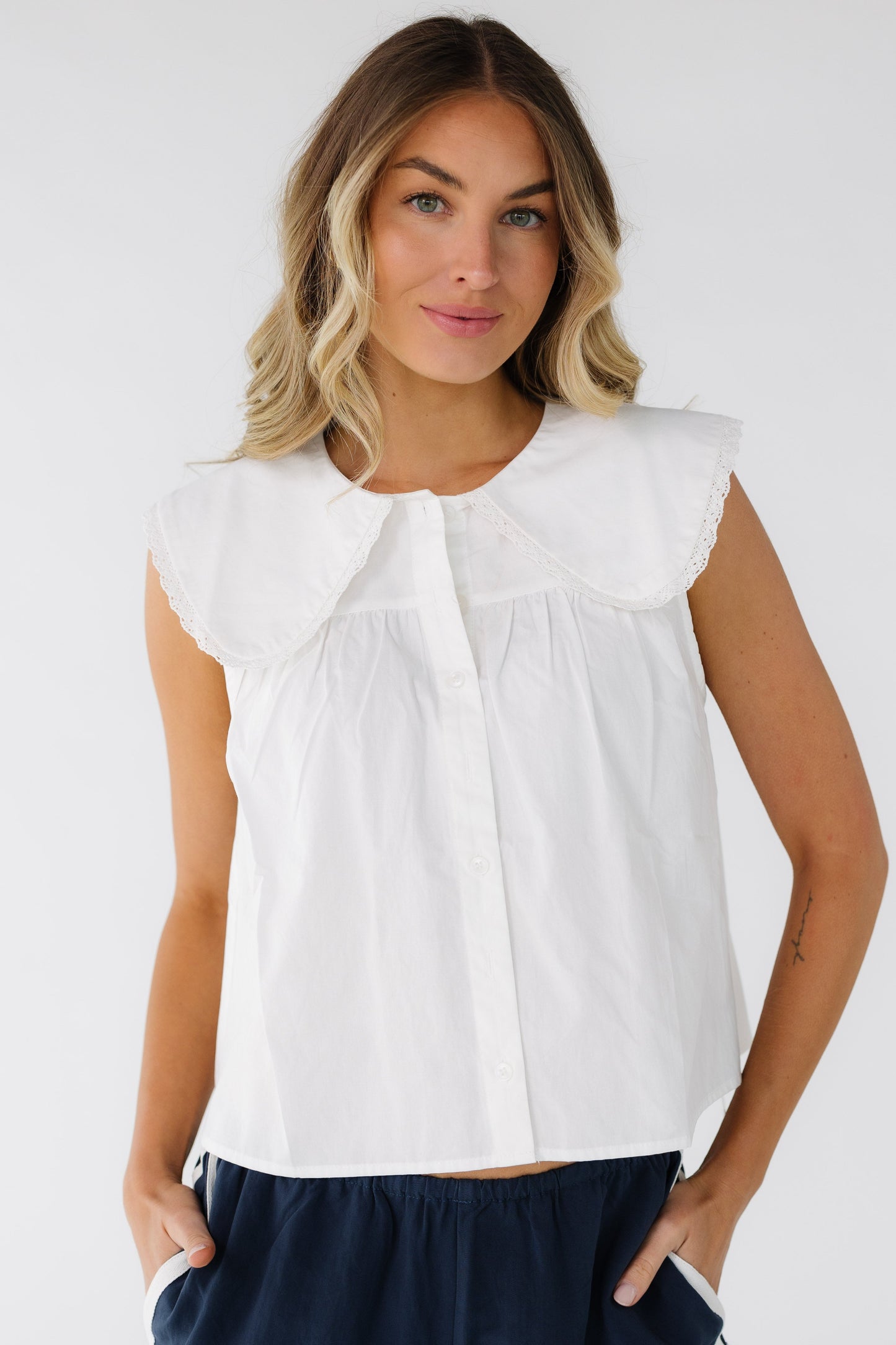 Young woman a sleeveless white button down blouse with a wide lace trimmed collar.
