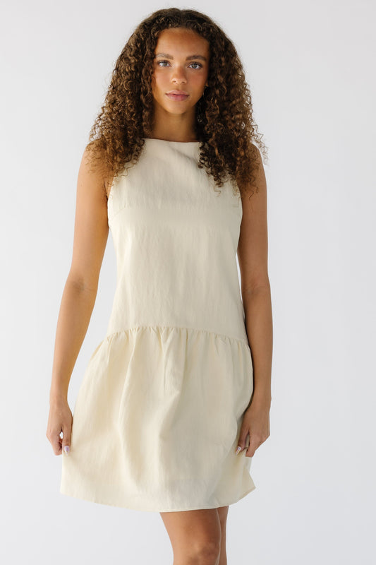 Teenage girl wearing a light yellow sleeveles dress with a sheath cut bodice and a gathered drop waist skirt.