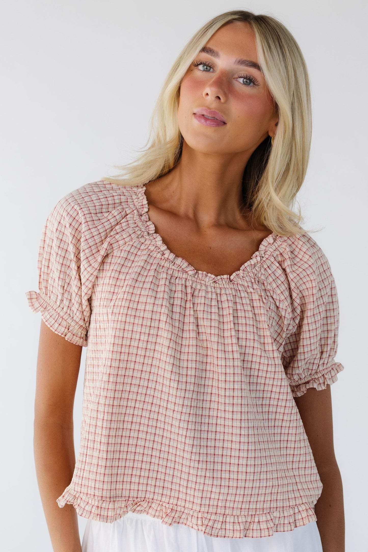 Woman wearing a red plaid blouse with short puff sleeves, a ruffled scoop neckline and a narrow ruffled hem.