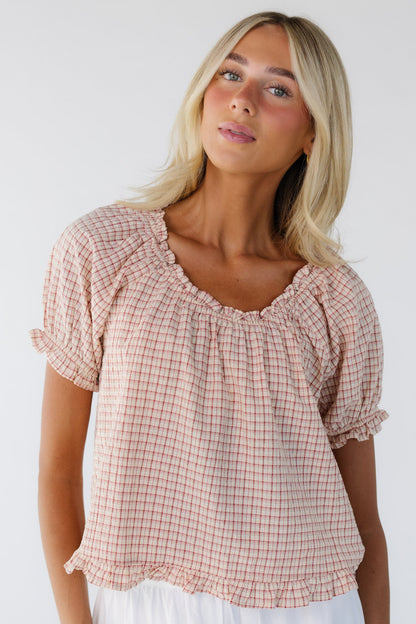 Woman wearing a red plaid blouse with short puff sleeves, a ruffled scoop neckline and a narrow ruffled hem.