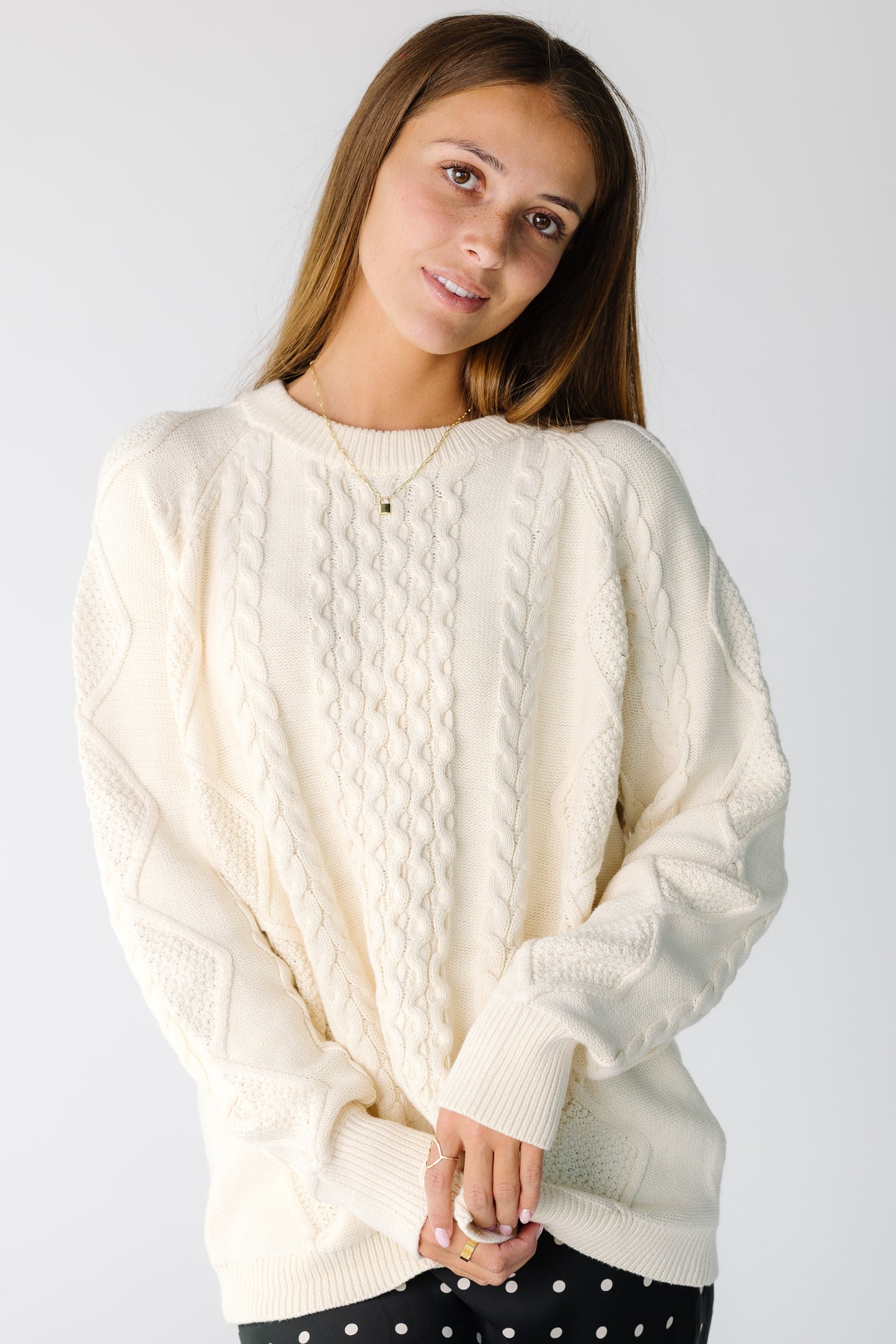 Woman wearing a modest white cable knit sweater with a crew neckline and long sleeves
