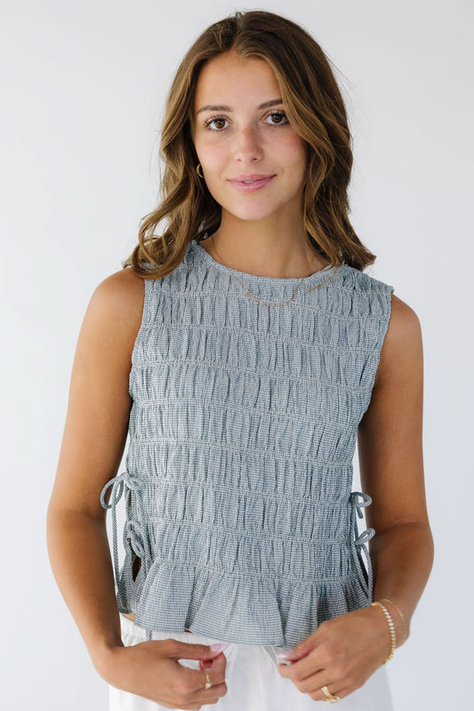 Young woman wearing a modest, sleeveless  blue and white gingham smocked top with 2 ties on each side.