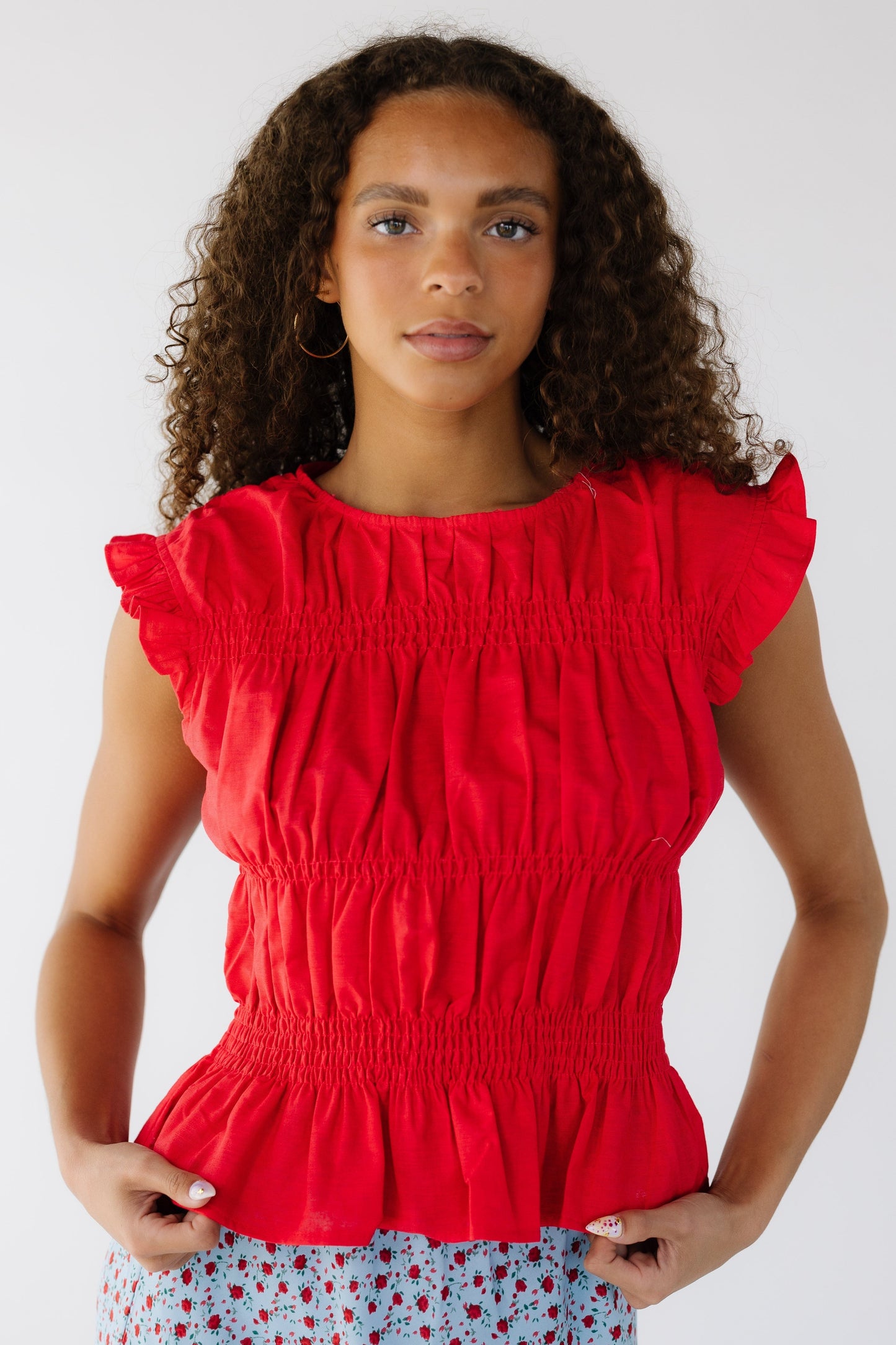 Teenage girl wearing a red, sleeveless, smocked blousy top.