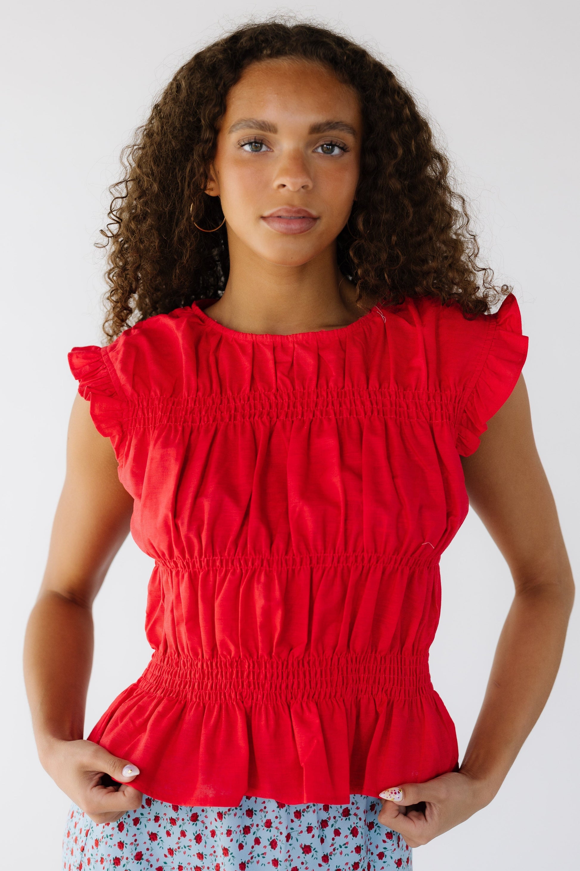 Teenage girl wearing a red, sleeveless, smocked blousy top.