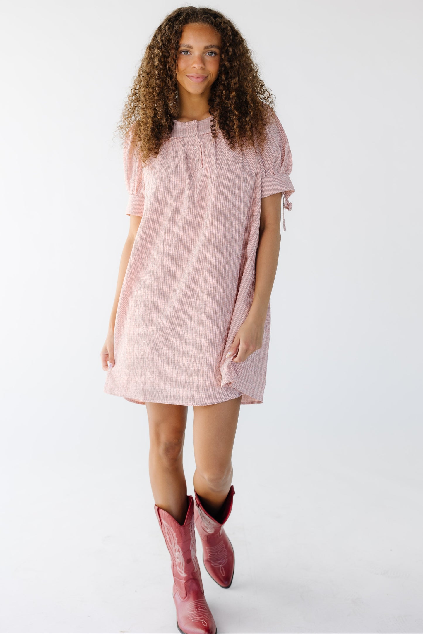 Teen girl wearing a modest textured pink gingham short dress with a round neckline and short puff sleeves.