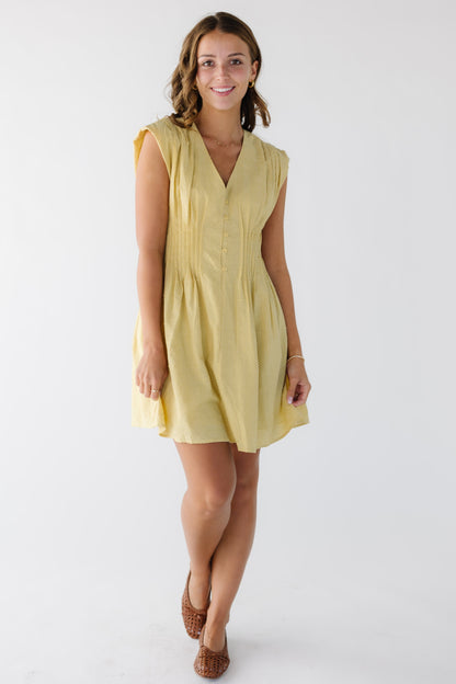 Young woman wearing a short, above the knee yellow polka dot, sleeveless dress with a V-neckline and pleats around the waist.