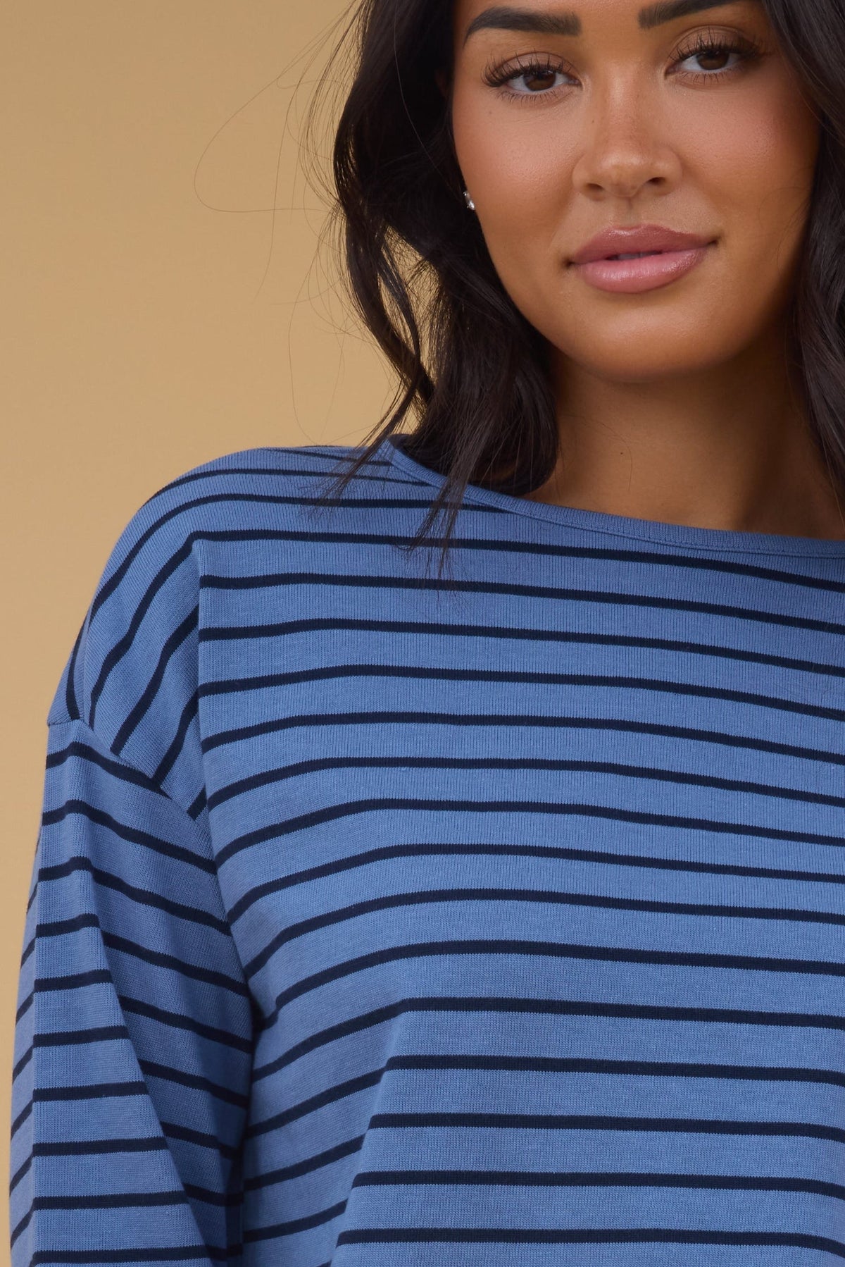 A close up view of a woman wearing a blue & navy stripe long sleeve tee.