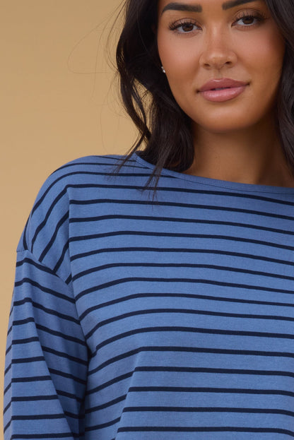 A close up view of a woman wearing a blue & navy stripe long sleeve tee.