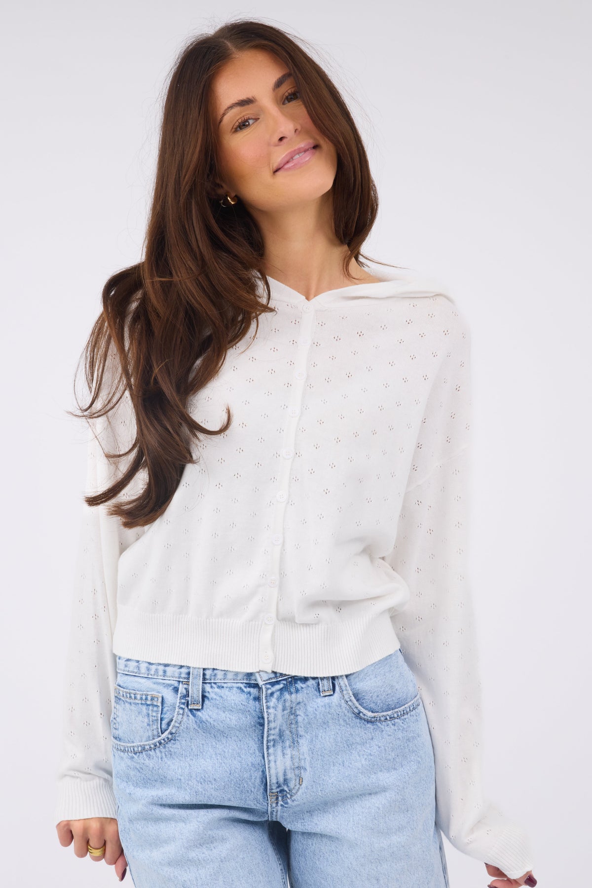 A young woman wearing a modest white pointelle knit, button down top with long sleeves and an attached hood.