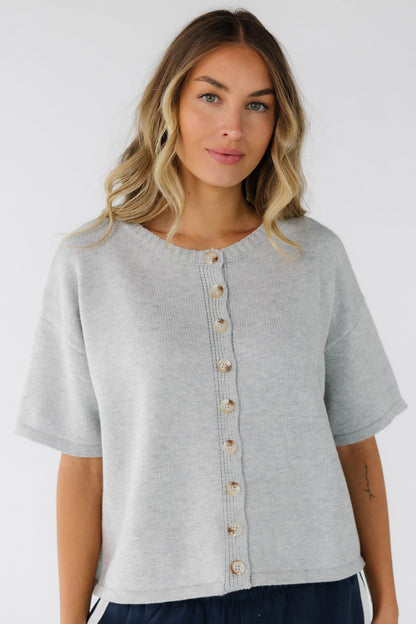 Young woman wearing a grey button down cardigan with a crew neckline, short sleeves and a boxy cut.  