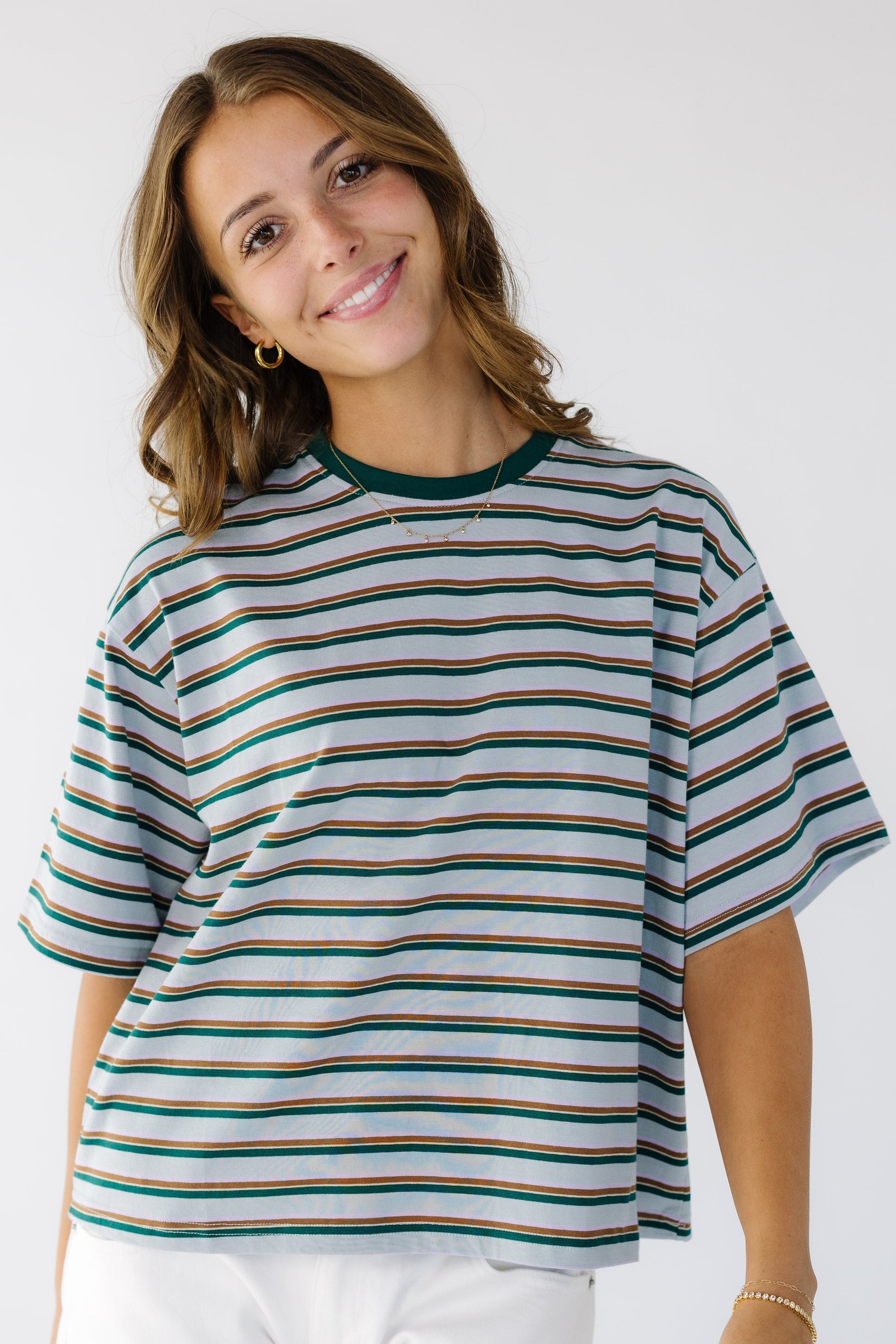 Young woman wearing a modest light blue short sleeve tee with brown and green paired stripes and a crew neckline.