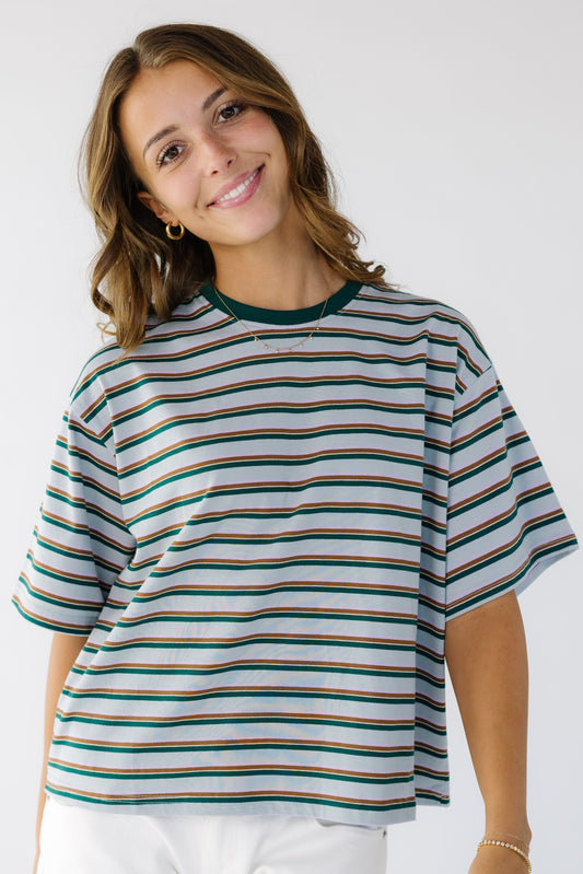 Young woman wearing a modest light blue short sleeve tee with brown and green paired stripes and a crew neckline.