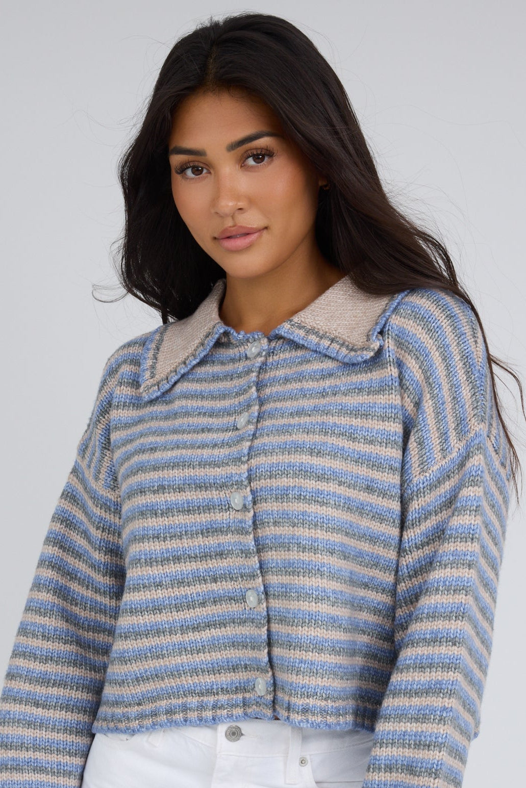 Young woman wearing a taupe-blue multi stripe cardigan with a pointed collar and long sleeves.