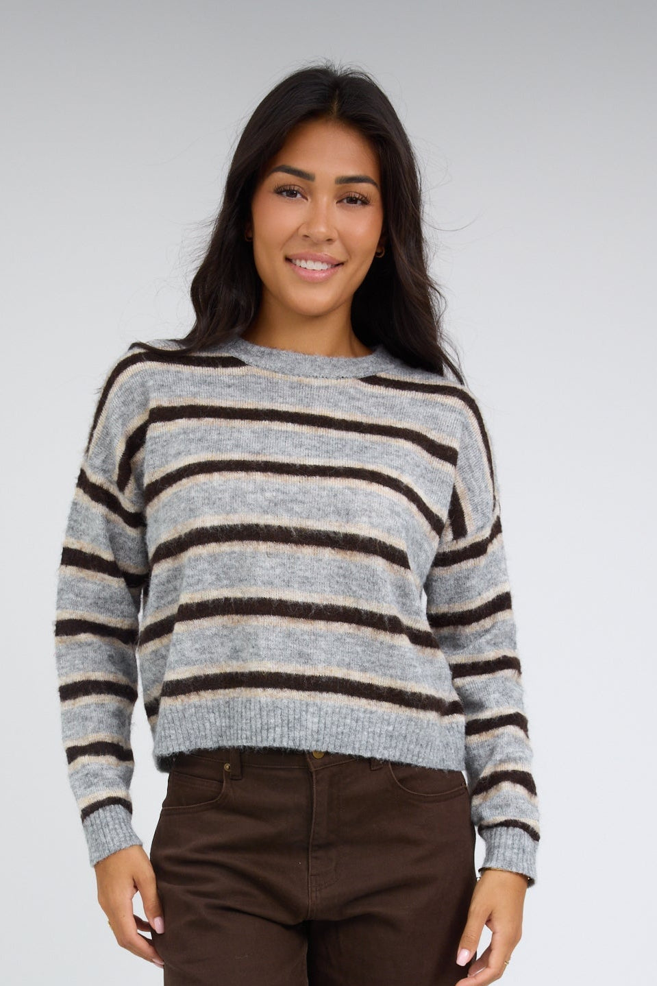 Young woman wearing a grey & brown multi color & stripe pullover with a crew neckline and long sleeves.