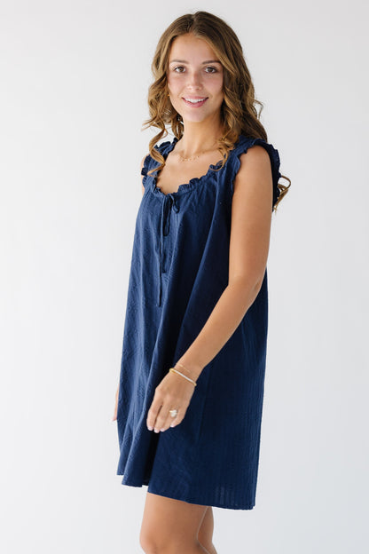 Side view of a woman wearing a navy textured swing dress with ruffle details at the neck and armholes.