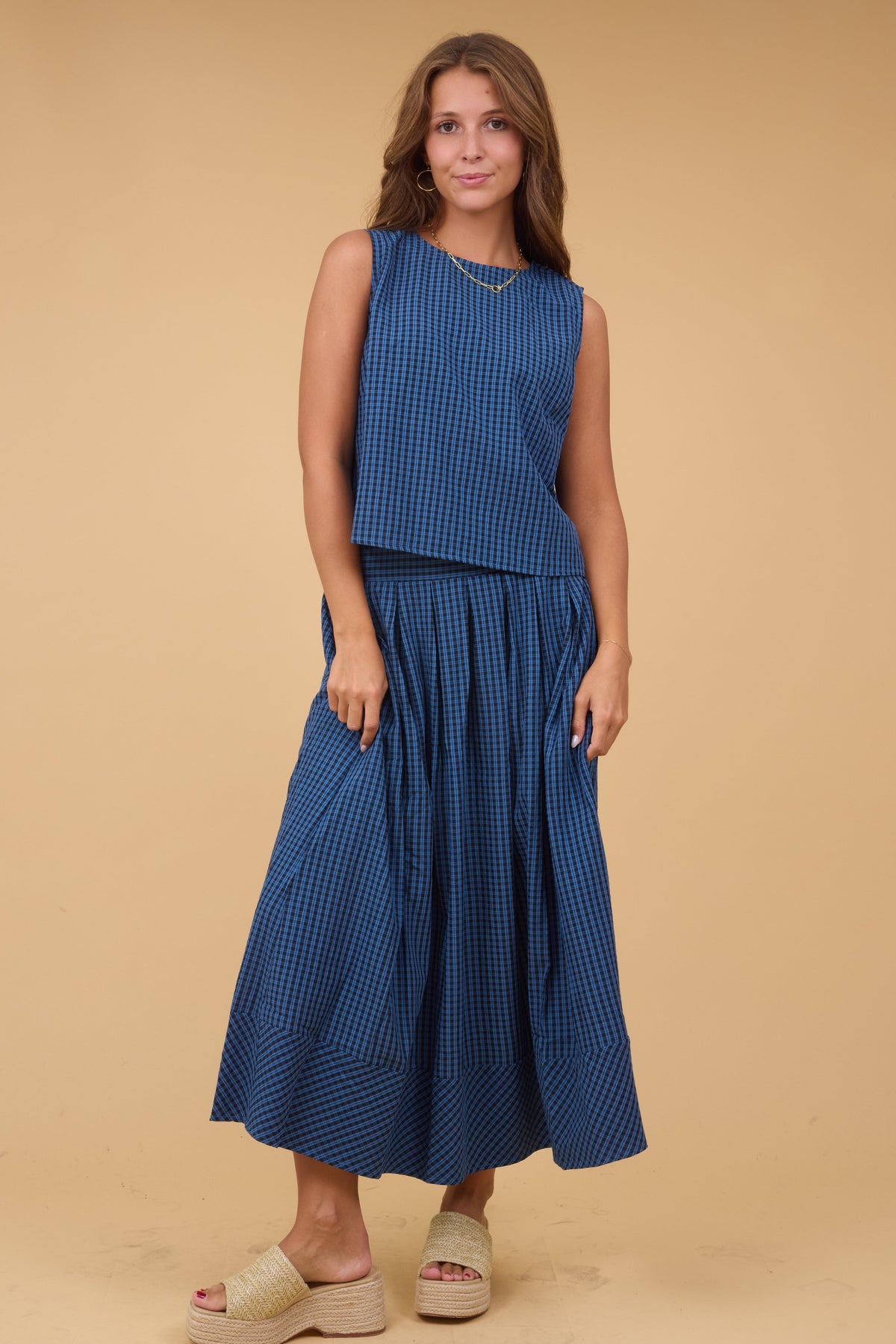 A woman wearing an blue & black plaid skirt & blouse set wth a sleeveless top & a full pleated skirt.