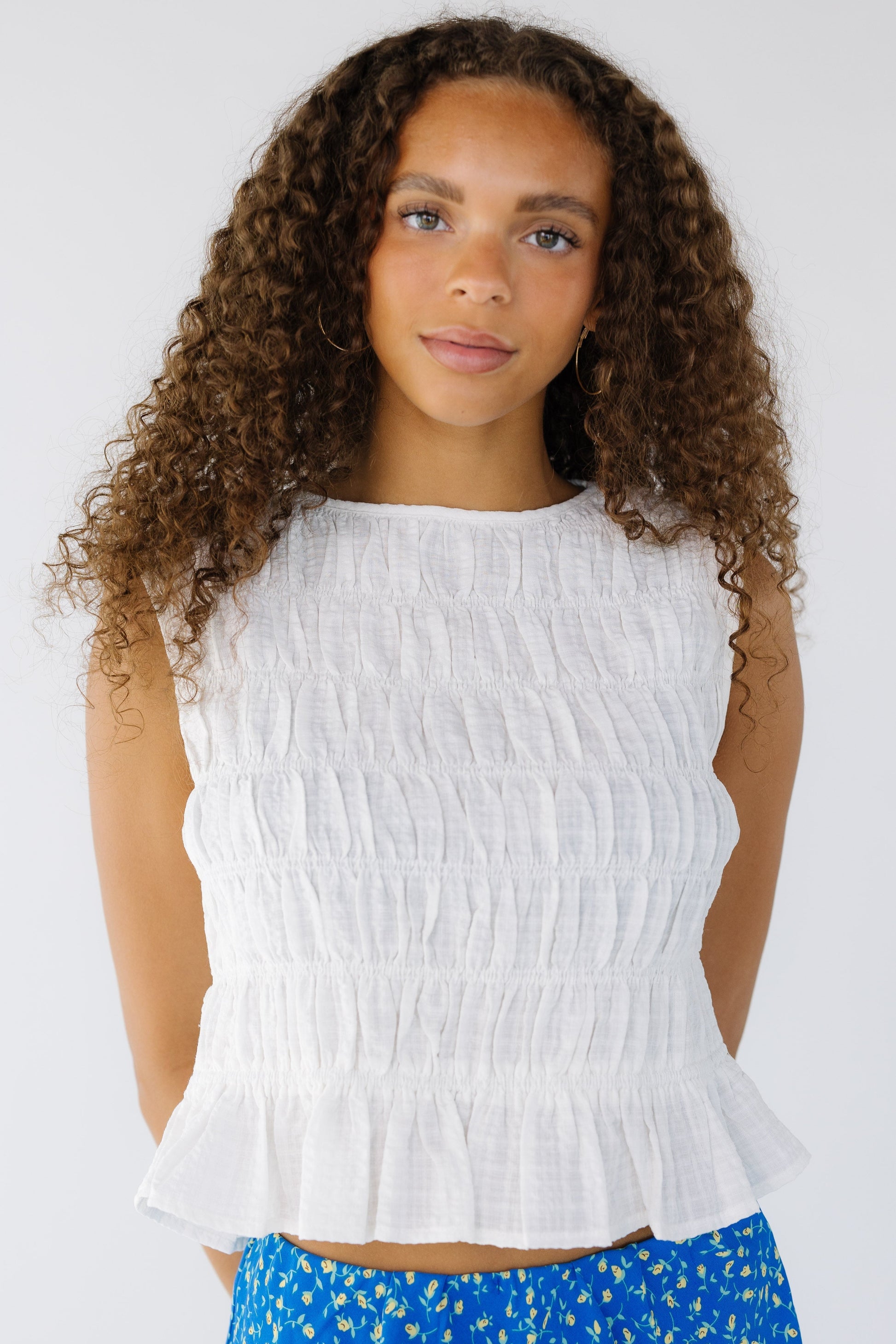 Teen girl wearing a modest white, sleeveless,  smocked blouse with a round neckline and a bottom ruffle.