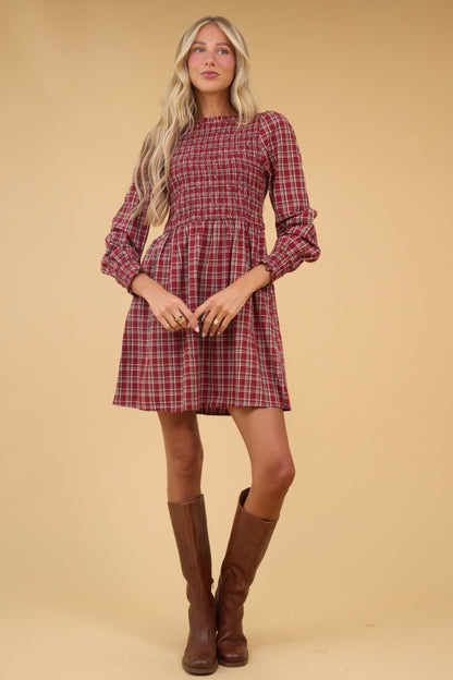 Woman wearing  red plaid dress with long sleeves, smocked bodice and full skirt.