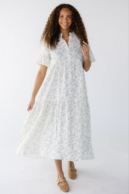 Young woman wearing a modest white and blue floral, loose fitting midi dress with short sleeves and a V-neckline.