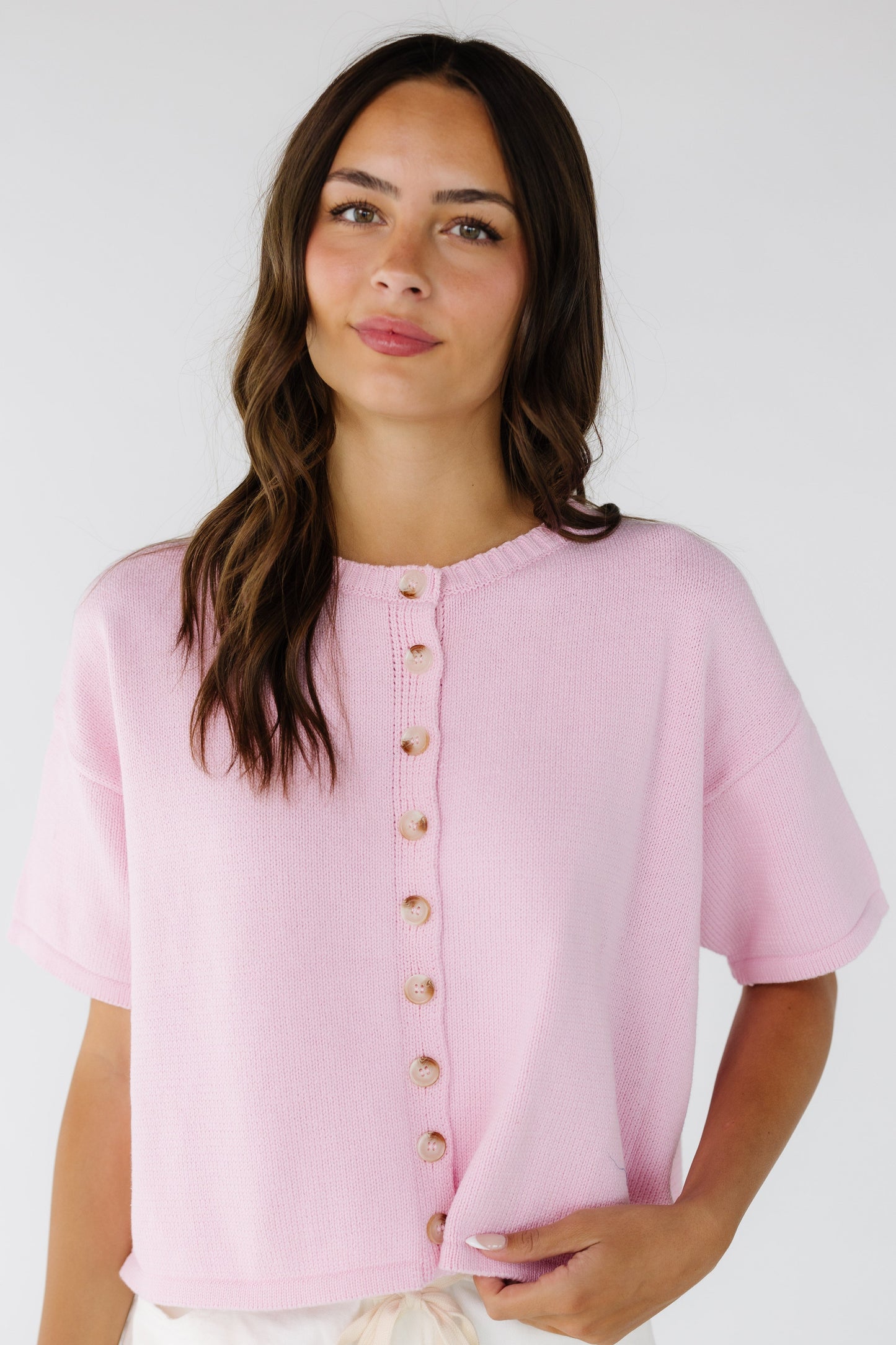 Young woman wearing a pink button down cardigan with short sleeves.