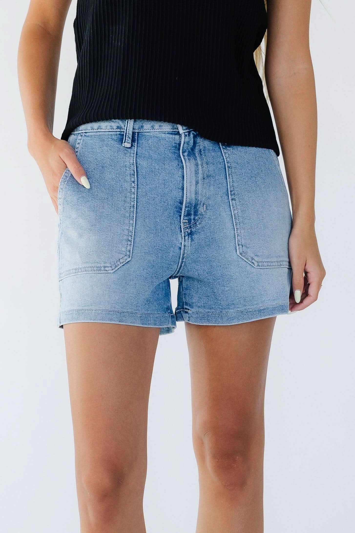 Young woman wearing light denim shorts with large front patch pockets and a button & zipper closure.