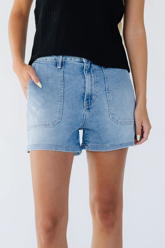 Young woman wearing light denim shorts with large front patch pockets and a button & zipper closure.