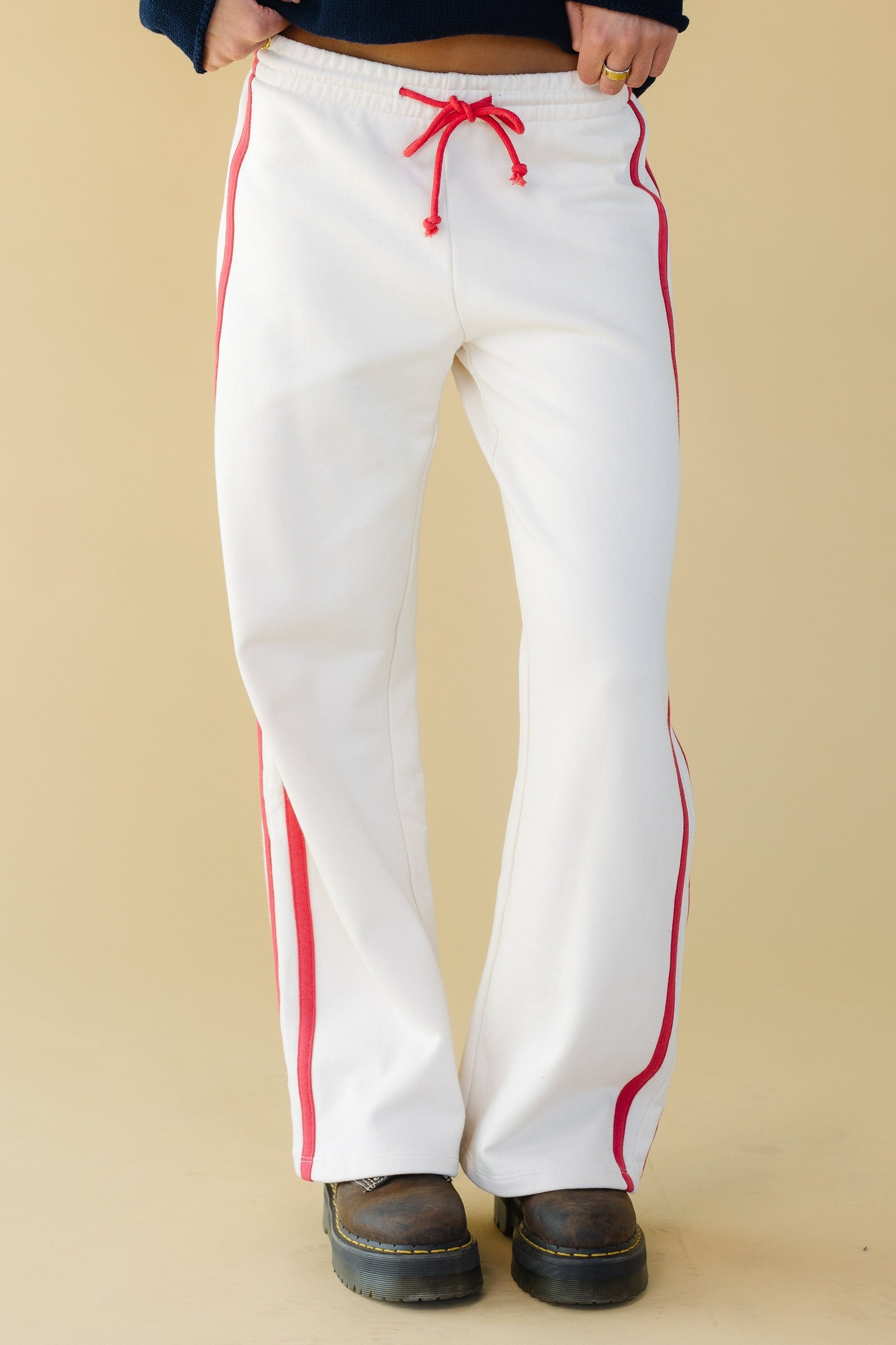 Woman wearing comfy white wide leg lounge pants with an elastic and drawstring waist and double red stripes down the side.