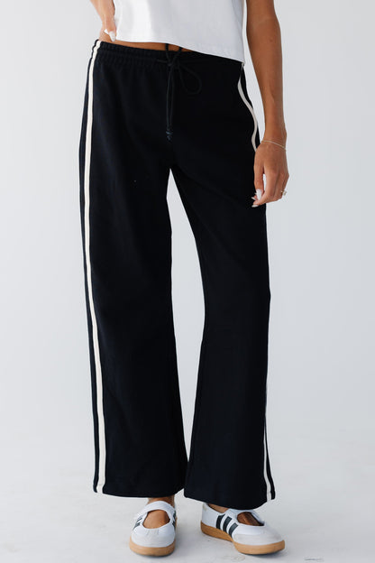 Young woman wearing a pair of loose fitting joggers with 2 white stripes down the side.