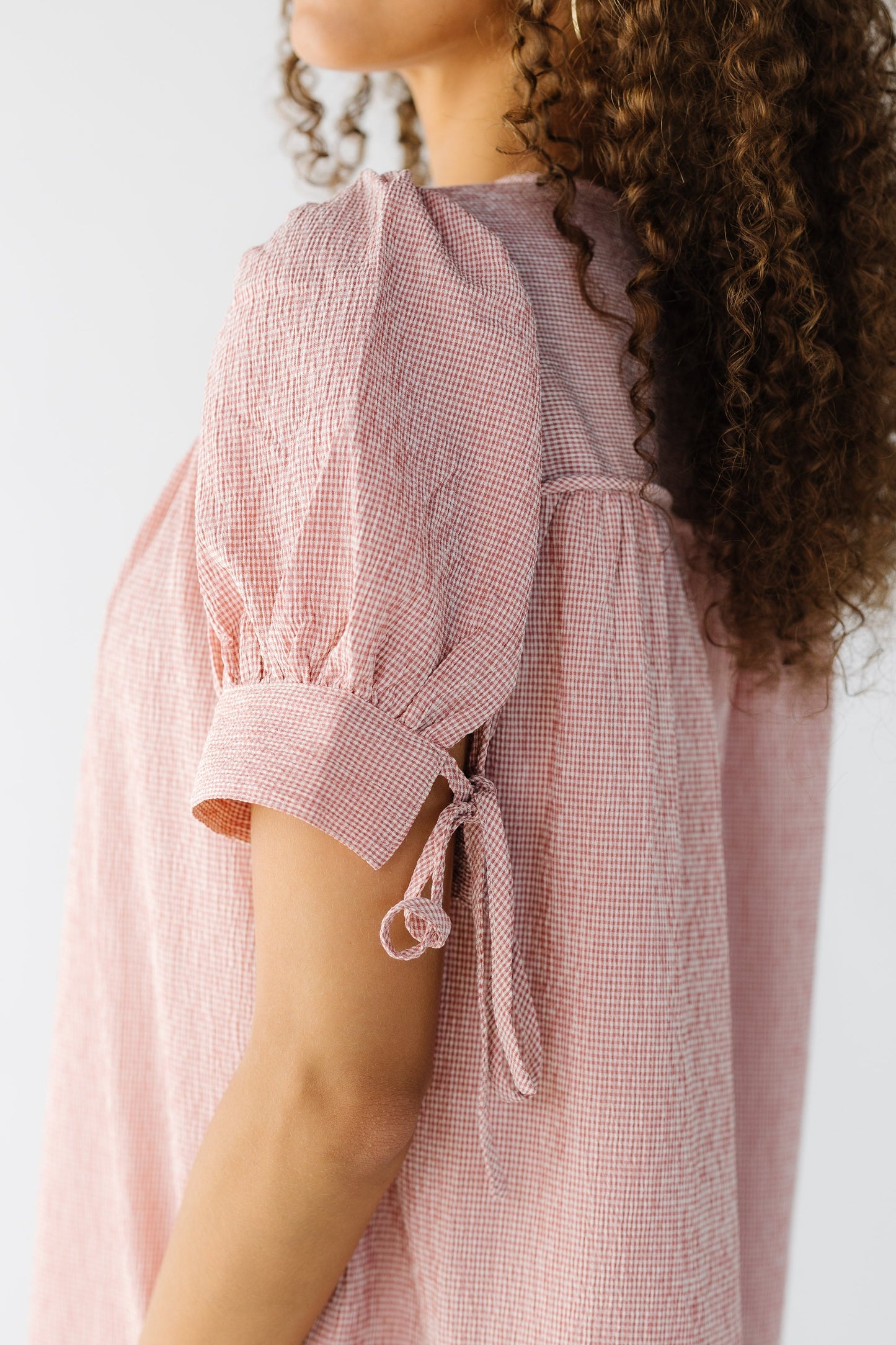 Close view of a teen girl wearing a pink gingham dress with a short puff sleeve with a wide cuff and tie back closure.