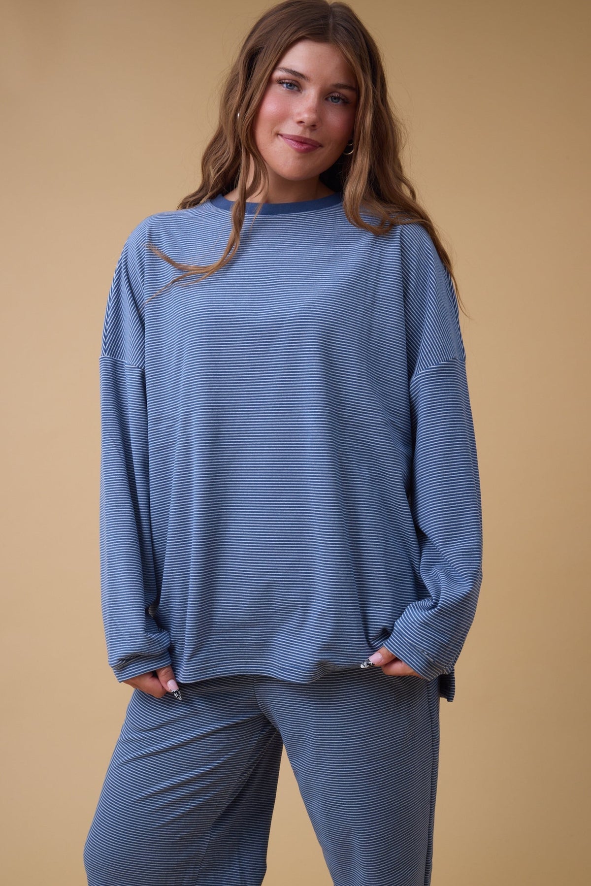 Young woman wearing a blue stripe lounge set with long sleeves and long wide pant legs.