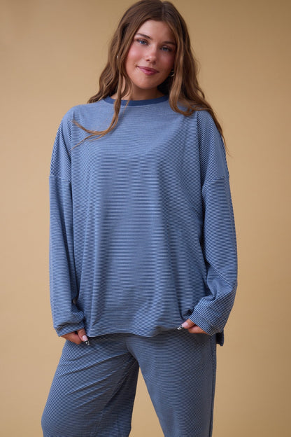 Young woman wearing a blue stripe lounge set with long sleeves and long wide pant legs.