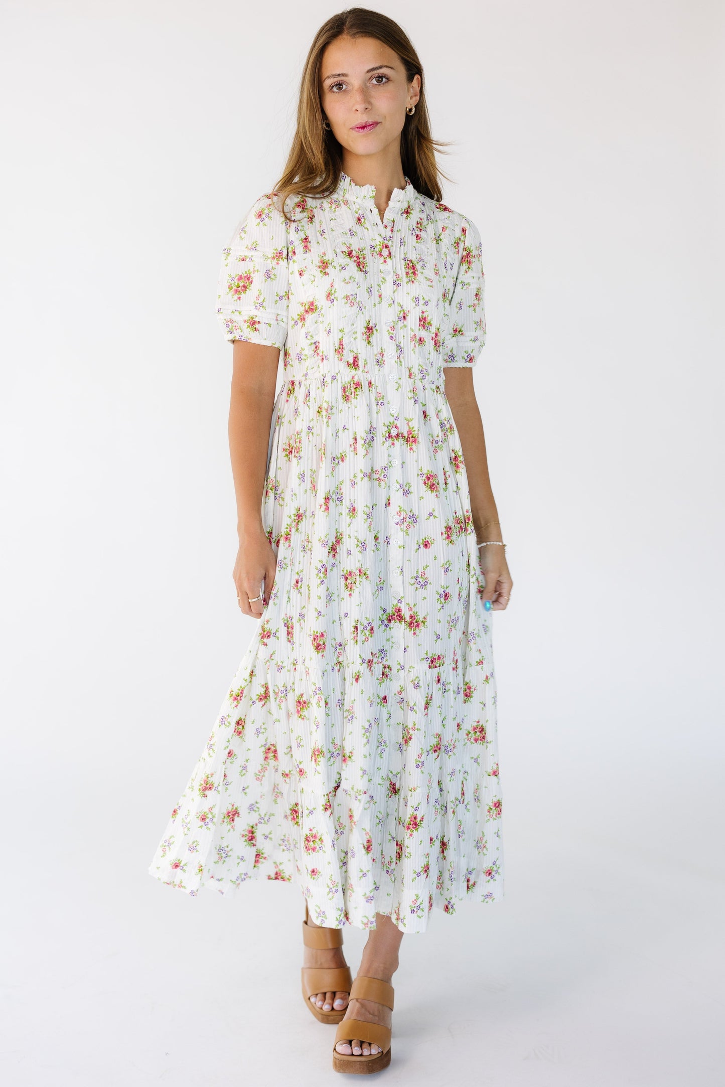 Woman wearing a white floral print dress that buttons down the full length of the dress with short puff sleeves and a high ruffle collar.