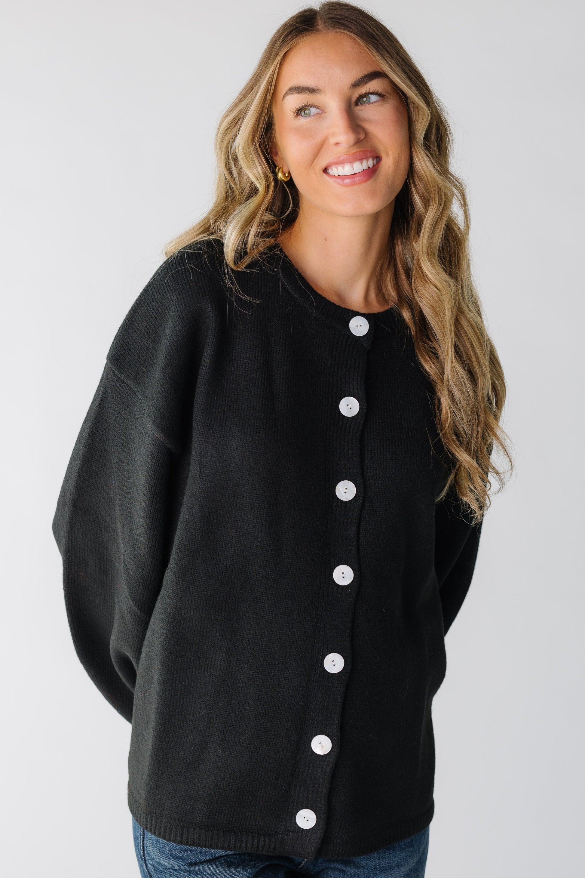 A woman wearing a black cardigan with large white buttons