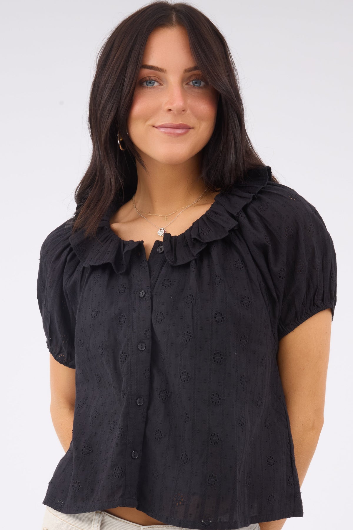 A young woman wearing a black eyelet button down blouse with short puff sleeves and a round ruffled collar.