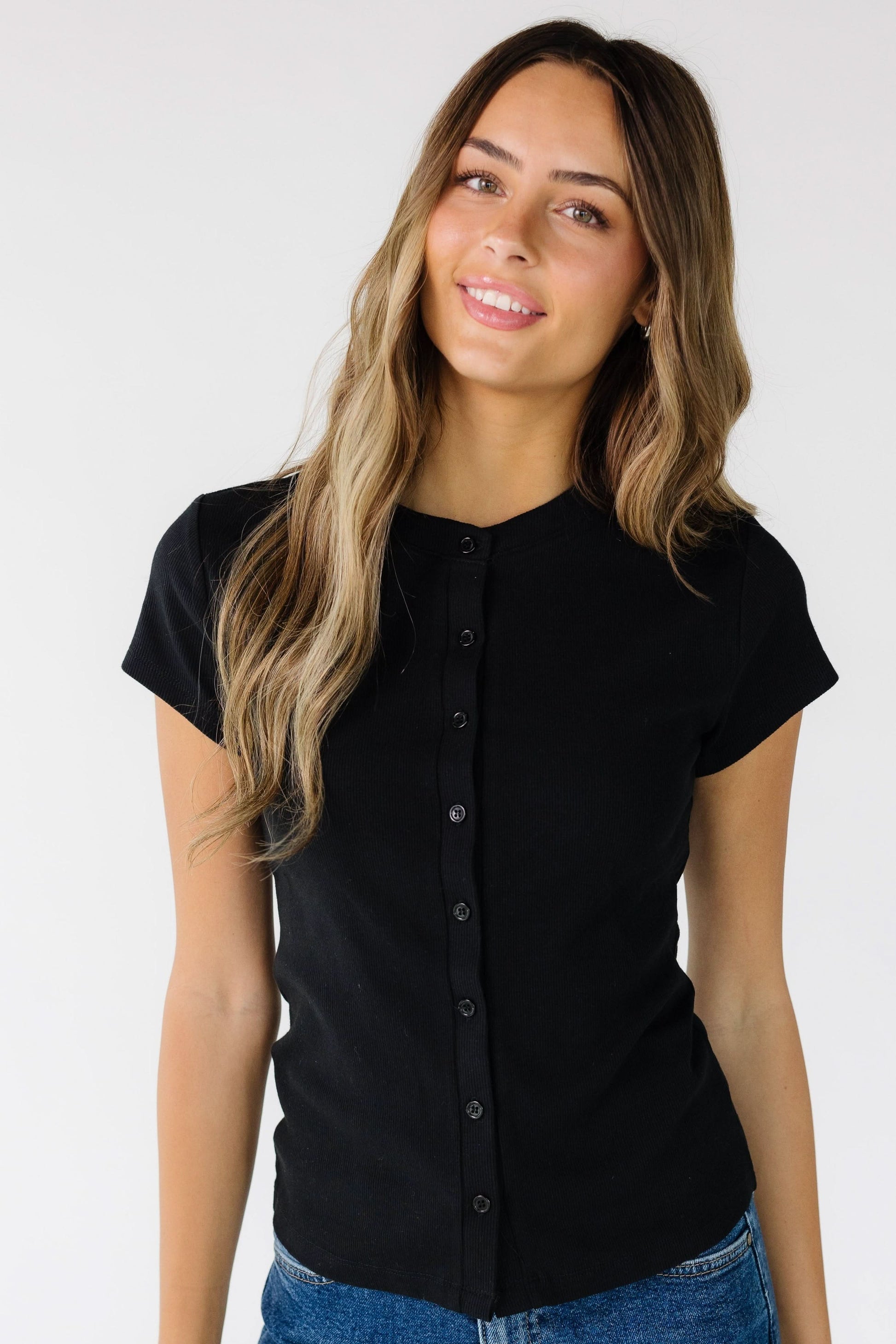 Young woman wearing a black button down top with short sleeves.