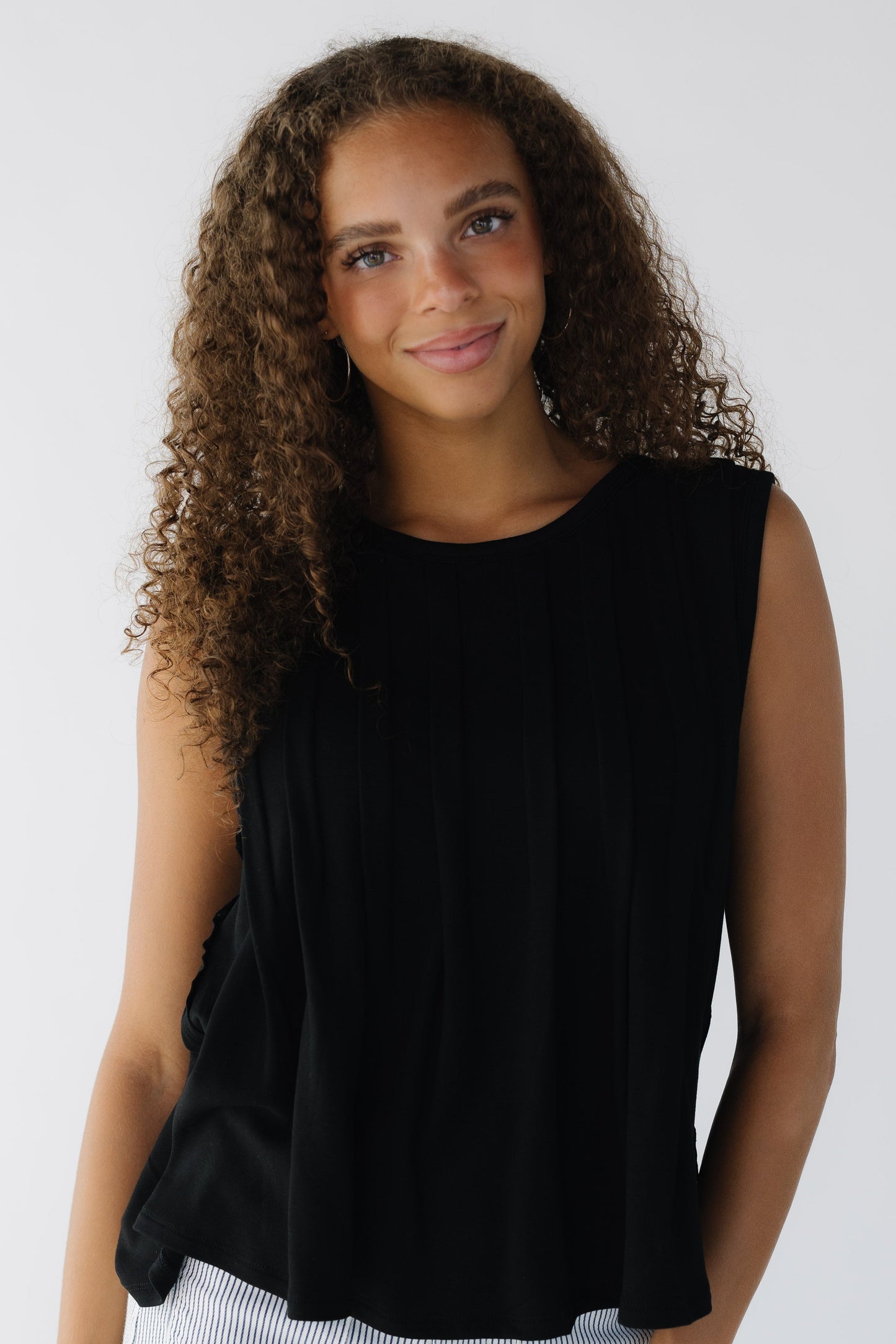 Teenage girl wearing a black sleeveless knit top with front pleats.