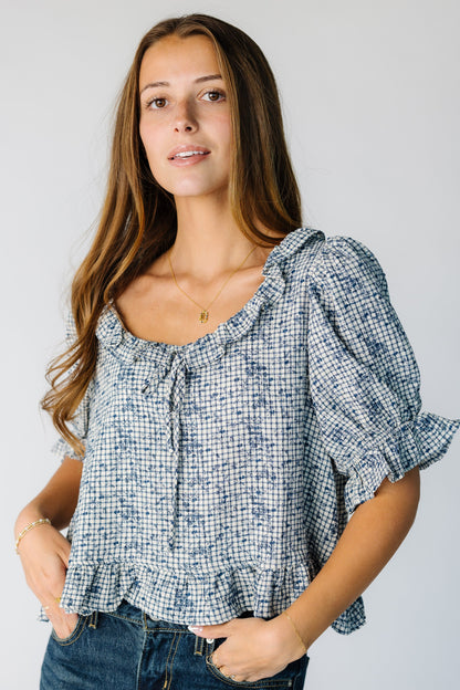 Woman wearing a blue plaid top with a scoop and ruffle neckline 
