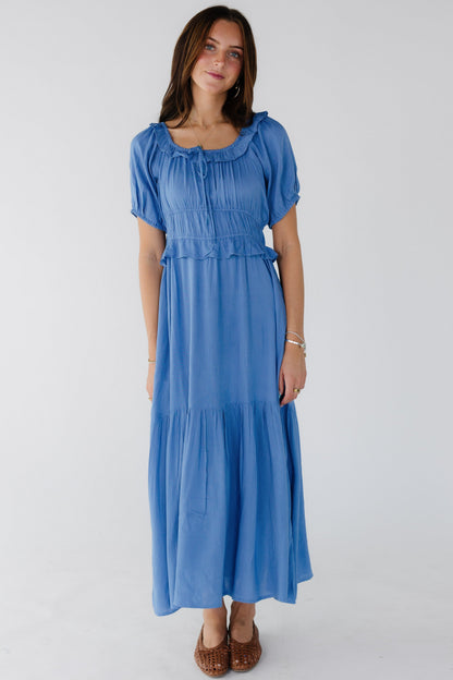 Woman wearing a blue polka dot midi dress with balloon sleeves, wide ruffled waist and a ruffled scoop neckline.