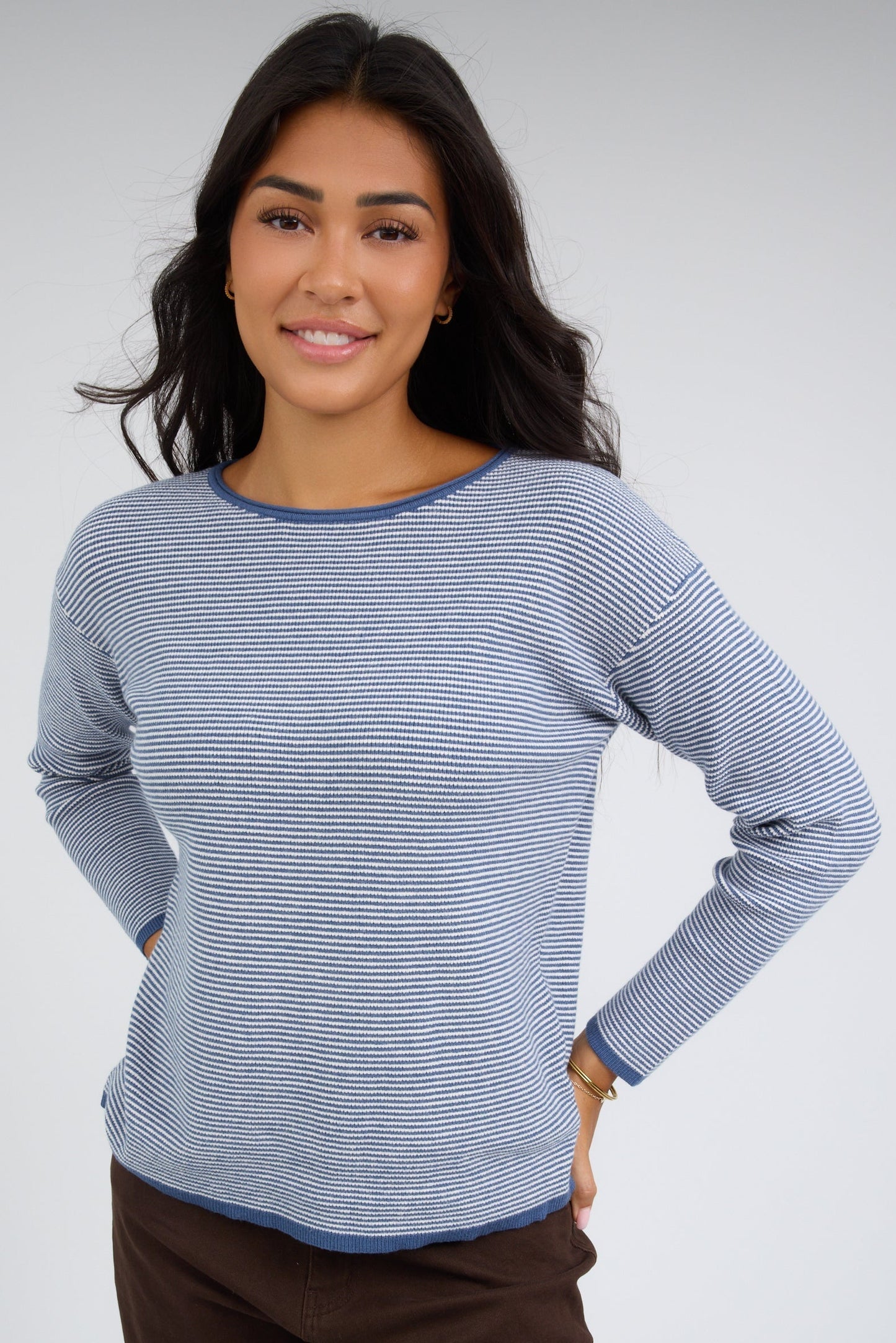 Young woman wearing a denim blue & white stripe, long sleeve top with a round neckline.