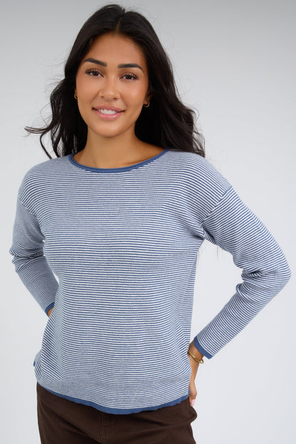Young woman wearing a denim blue & white stripe, long sleeve top with a round neckline.