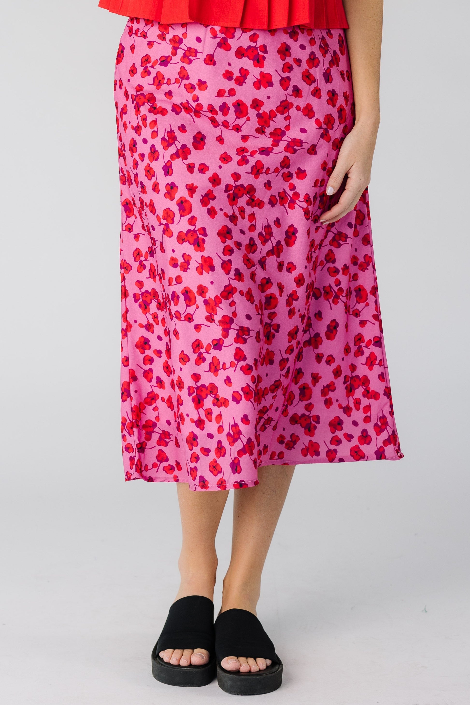 Woman wearing a pink A-line midi skirt with a red floral print.