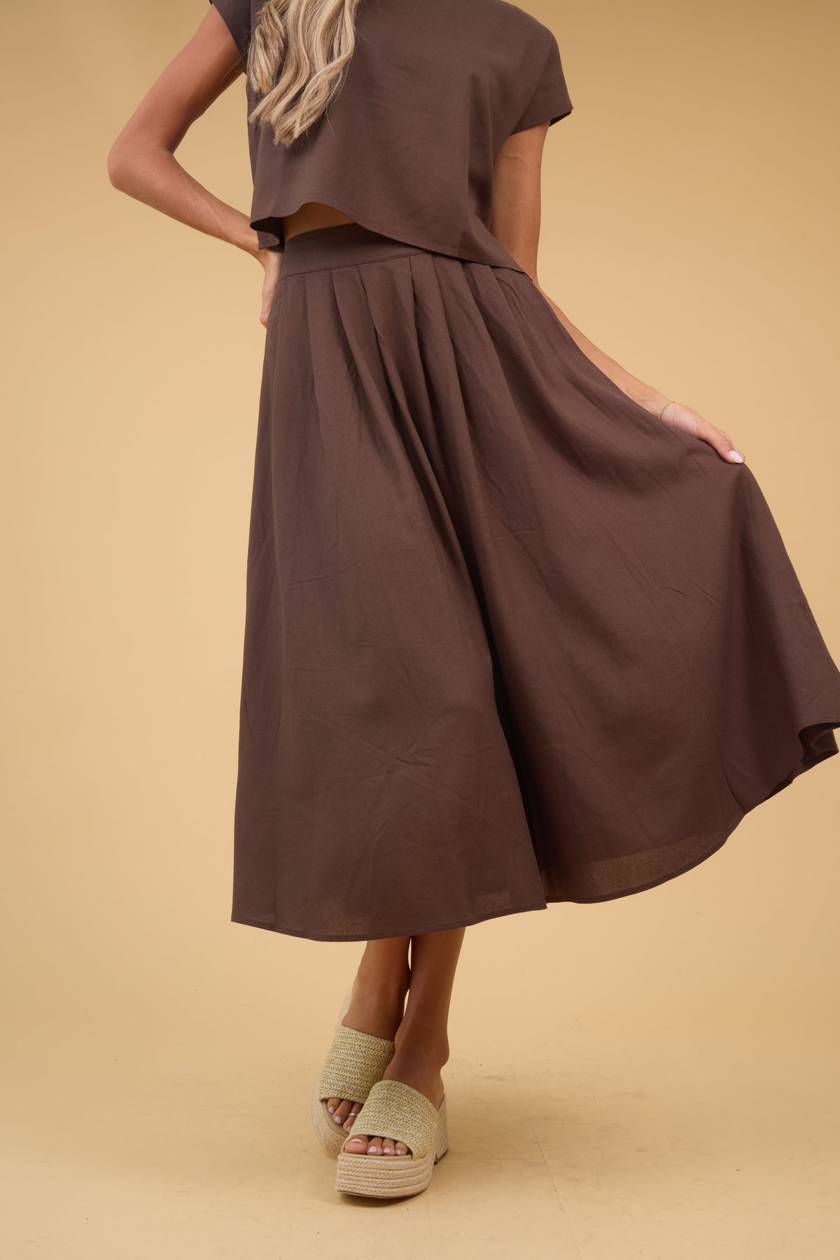 Young woman wearing a brown midi skirt with a wide waistband and front pleats.