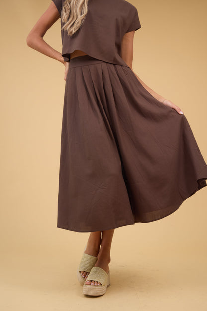 Young woman wearing a brown midi skirt with a wide waistband and front pleats.