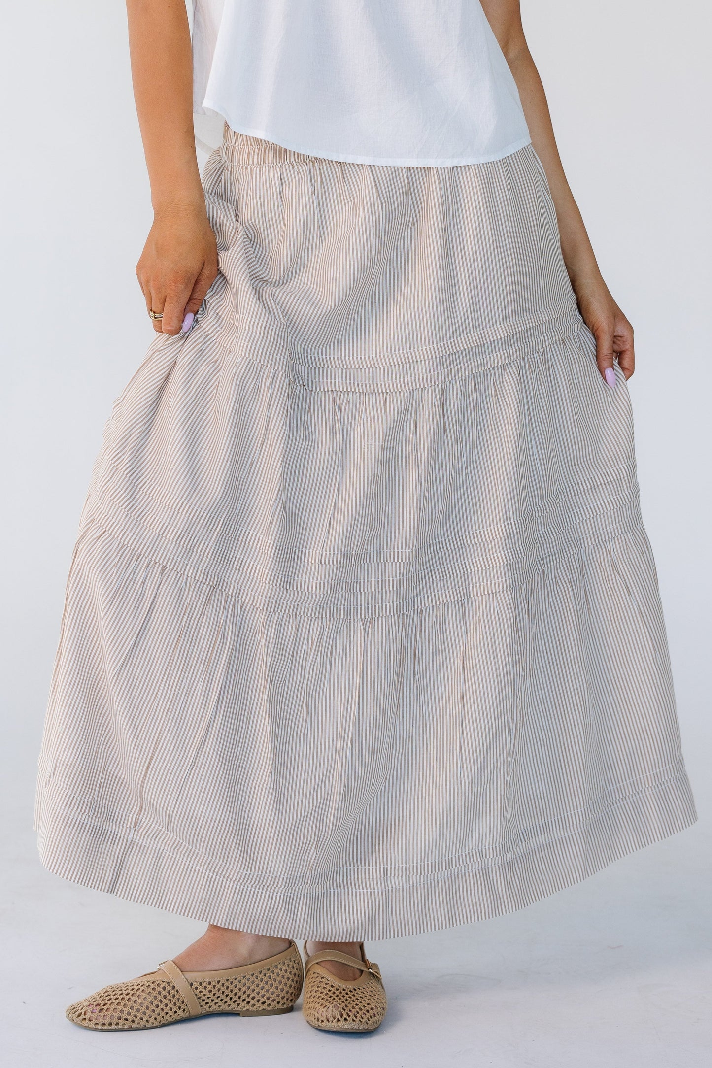 Woman wearing a camel vertical stripe skirt with horizontal pleats and 2 gathered tiers.