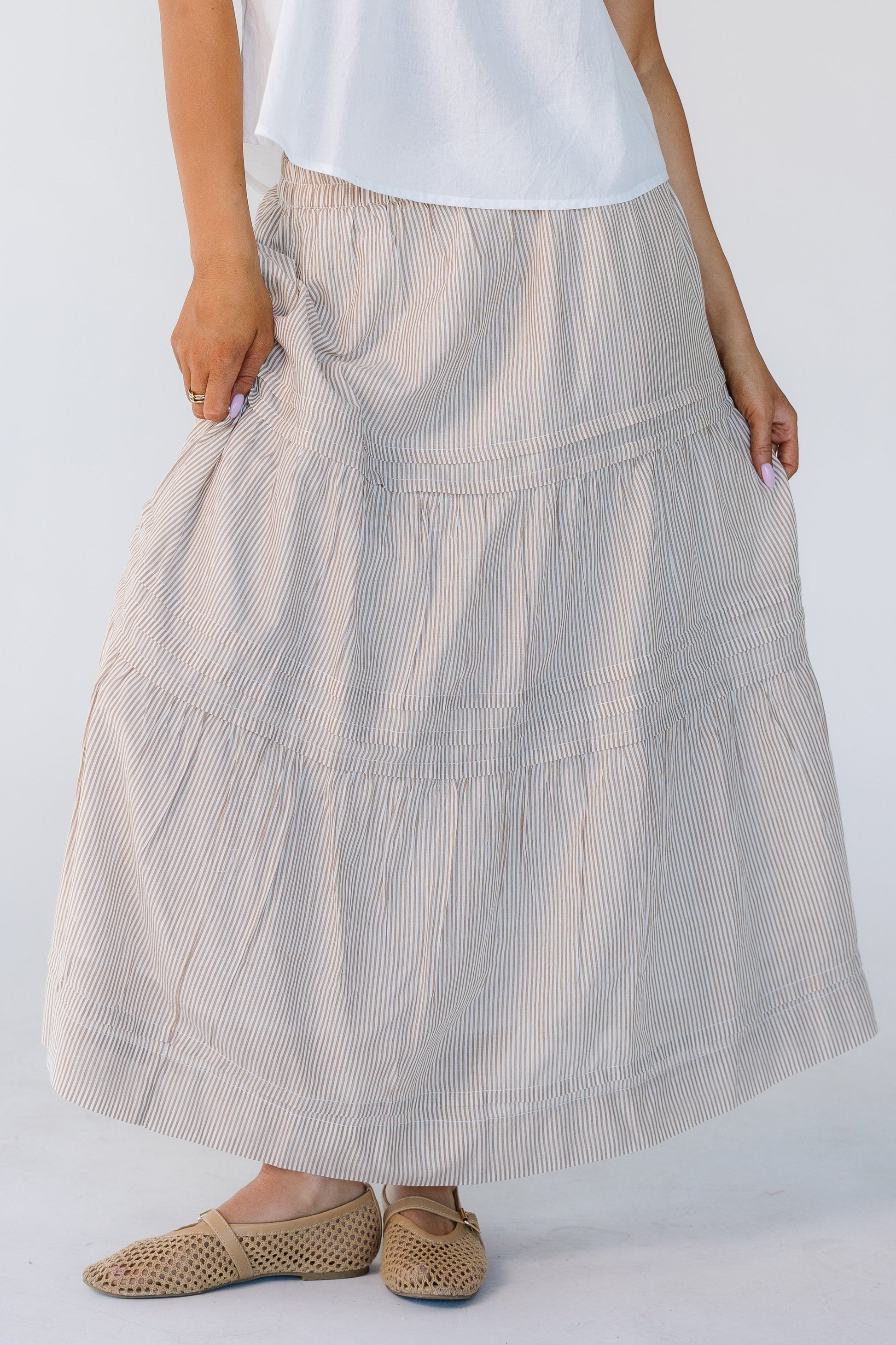 Woman wearing a camel vertical stripe skirt with horizontal pleats and 2 gathered tiers.